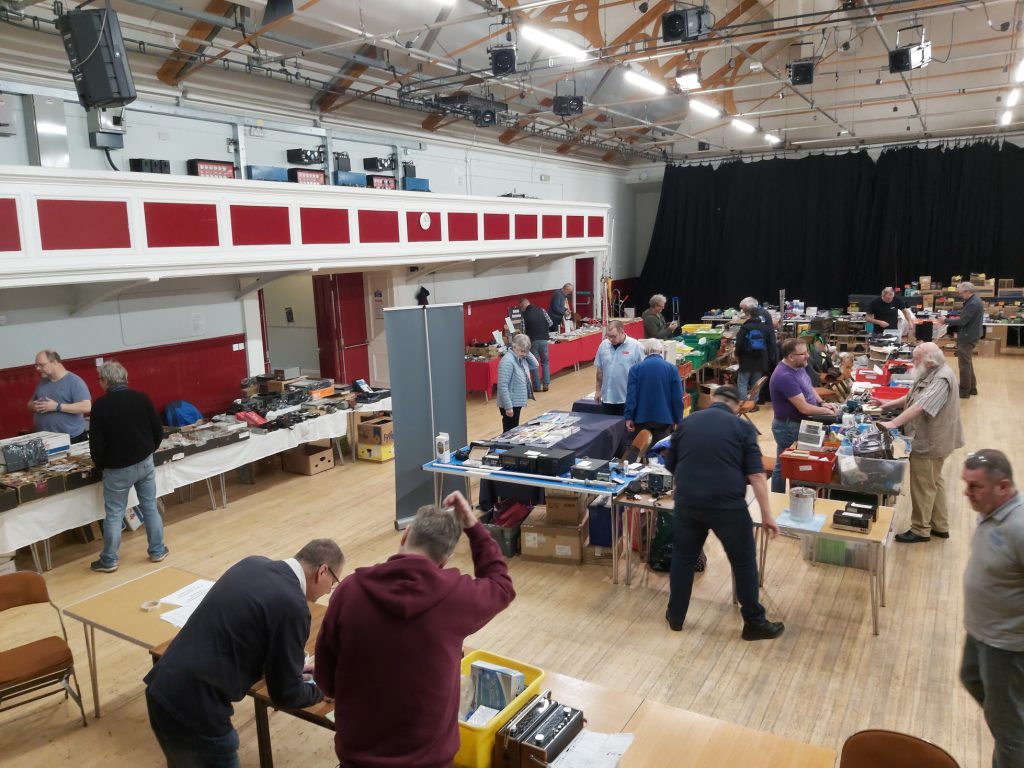 View across the hall from the stage, with traders stalls set up. Dave MM0HTL and John GM7NVA booking in early Bring and Buy items.
