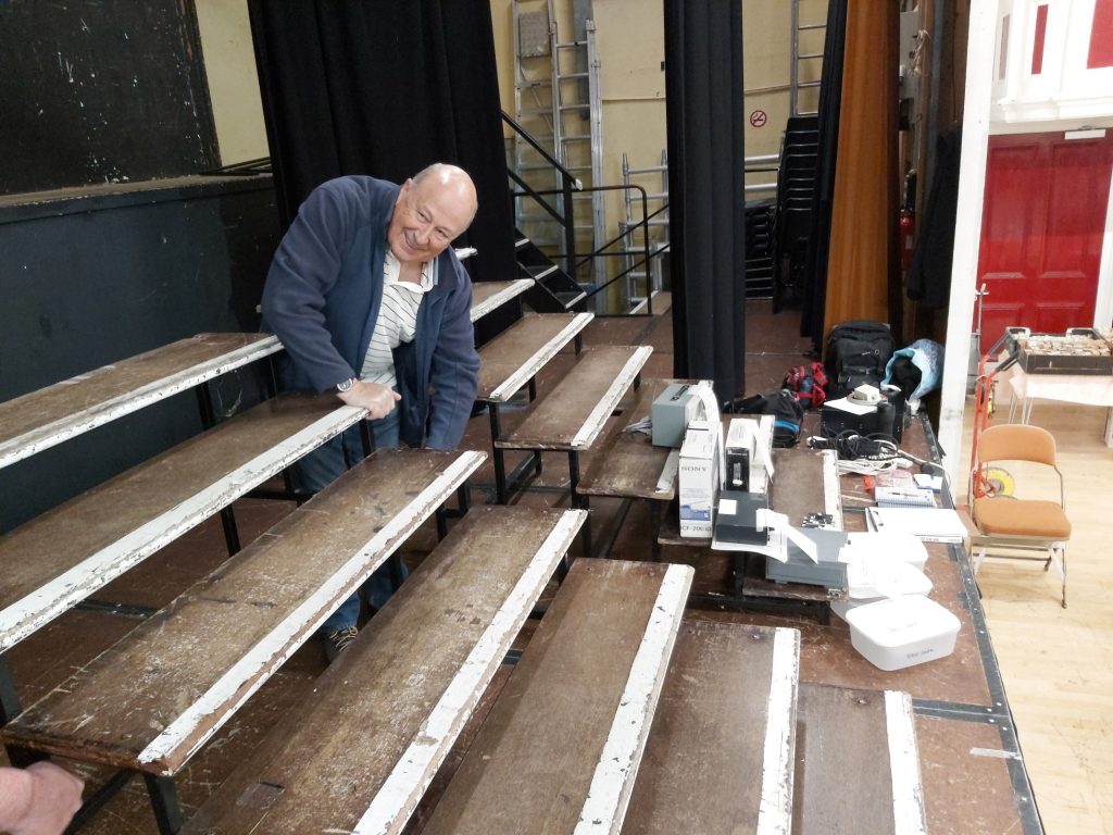 Dave GM0KCN setting up set of stage steps on the stage for use as shelving for Bring & Buy items