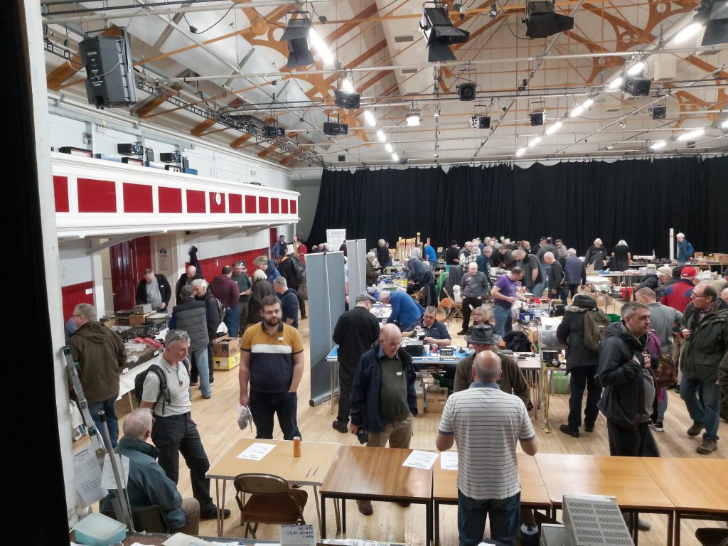 Looking across hall from the stage, full of people all around the traders tables